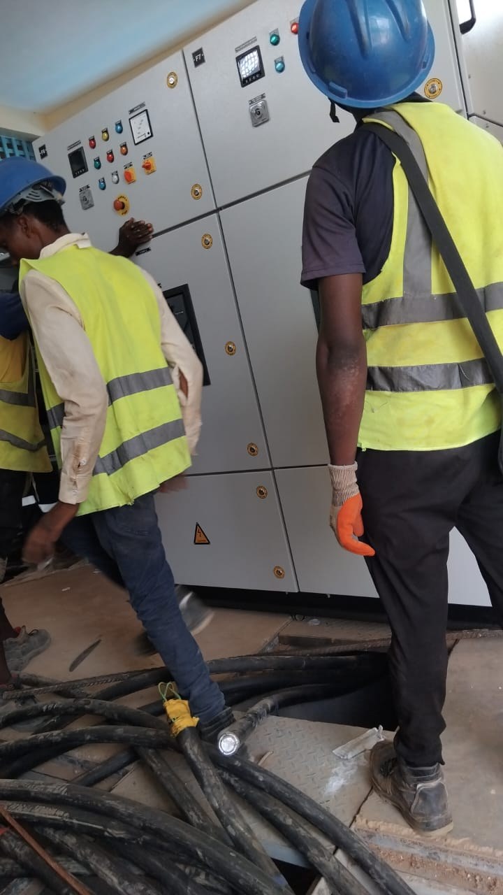 Technicians in safety vests working at a switchgear panel on site