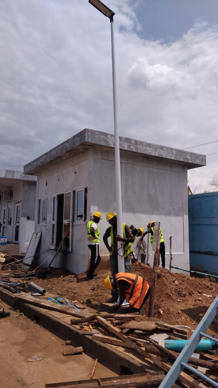 Crew in hard hats and hi-vis vests installing a street light pole beside a new building, Burkina Faso